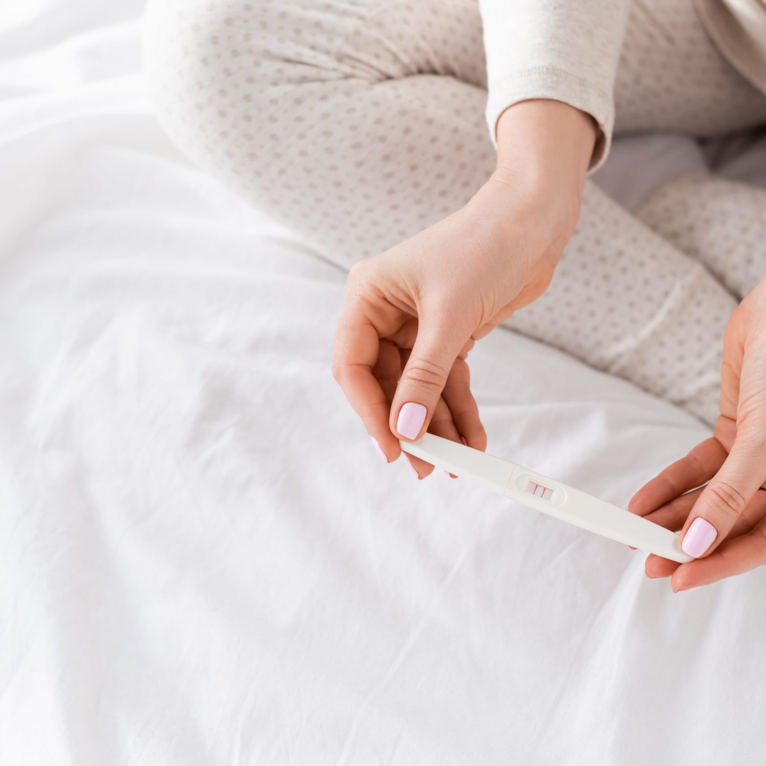 cropped view of woman holding pregnancy test in bedroom