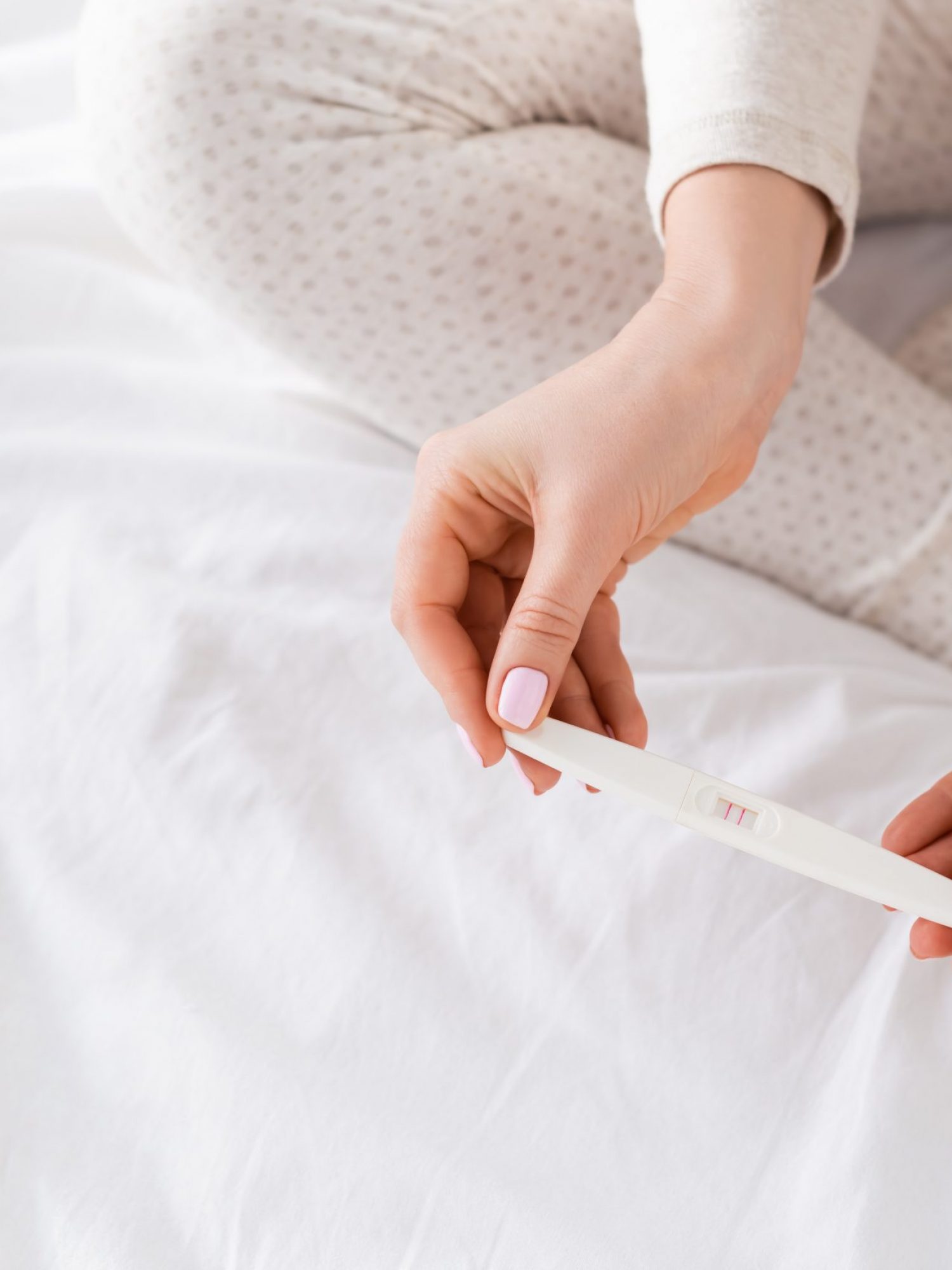 cropped view of woman holding pregnancy test in bedroom