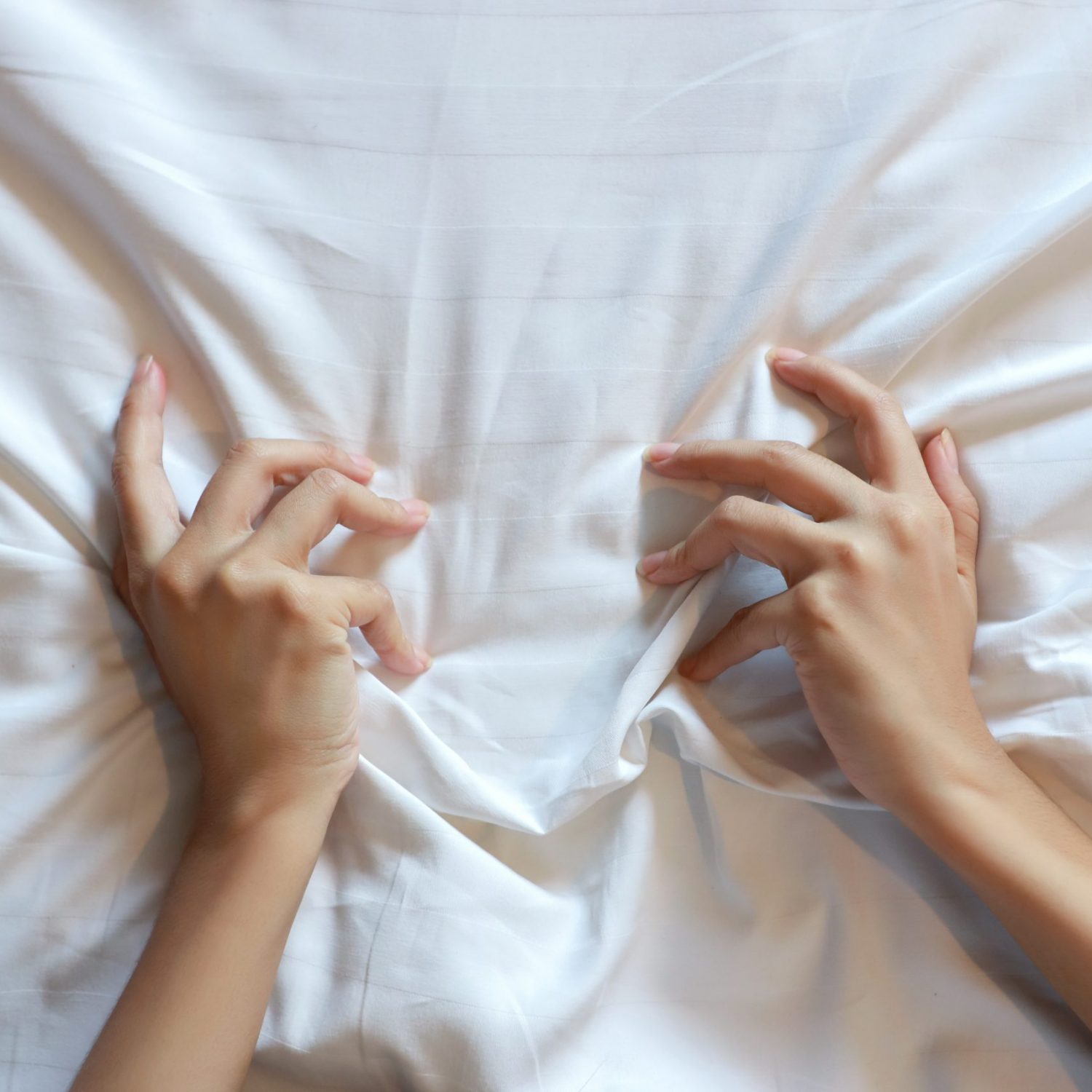Top view young sexy woman hands pulling white sheets in ecstasy in hotel. Cute girl doing sign orgasm on white bed, sex and erotic concept for advertisement